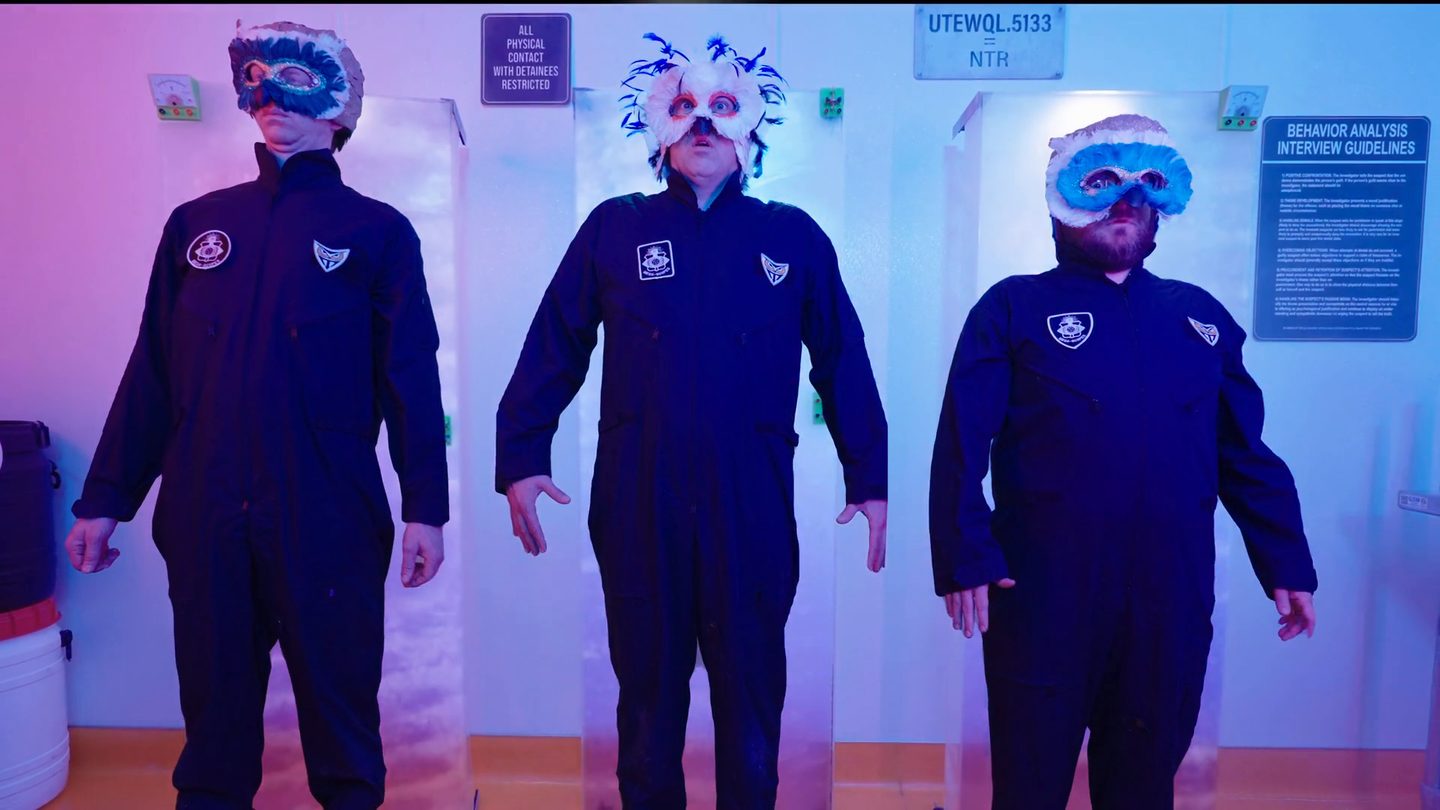 Three masked Owlien specimens standing in their containment pods